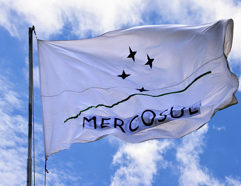 Mercosur: flag of the Mercosur / Mercosul trade bloc in the wind - four blue stars located in a curved green line, representing the constellation of the southern transept that emerges from the horizon - Mercosur's full members are Argentina, Brazil, Paraguay, and Uruguay, Venezuela has been suspended since 2016, associate countries are Bolivia, Chile, Colombia, Ecuador, Guyana, Peru and Suriname.