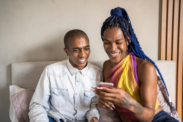 スマートフォンを使用して話すベッドでアフリカ系アメリカ人の非バイナリ人とトランスジェンダーの女性。lgbtカップル。 - trans ストックフォトと画像