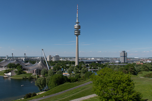 Munich, Germany - June 2, 2021: View of Olympiapark (Olympic Park) and the Olympiaturm (Olympic Tower; a broadcast tower) in early summer, with the BMW buildings (BMW Welt, tower, museum and plant) in the back, on the right.