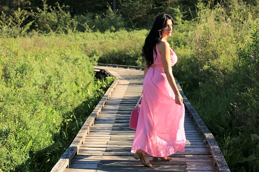 A model in a pink sleeveless dress holding a pose while walking on a boardwalk.