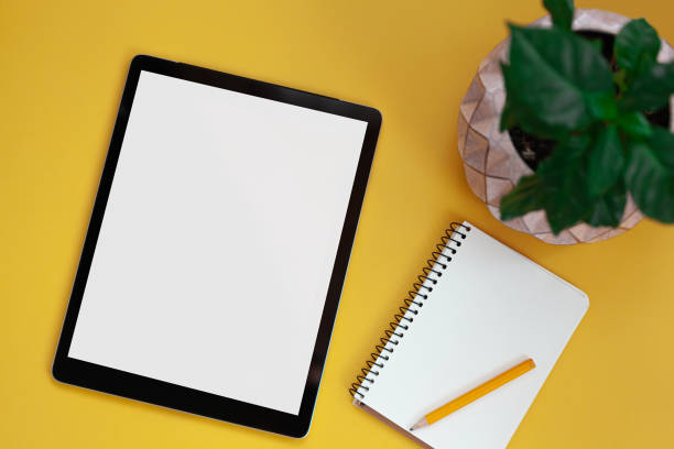 istock Tablet screen mockup and notepad isolated on yellow background, top view 1322192249