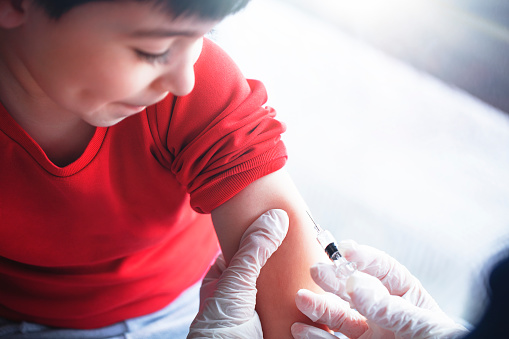 This picture depicts a young female clinician using a syringe to inject a concept COVD-19 liquid vaccine into a young boy patient during the Phase 3 vaccination human trials.