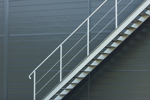 part of a large staircase with gray steps with metal handrails with a pattern against the black wall outside
