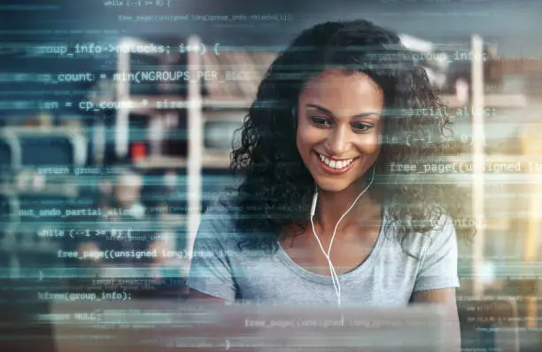 Photo of Digitally enhanced shot of an attractive businesswoman using a laptop superimposed over multiple lines of computer code