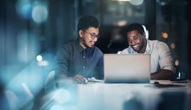 tiro cortado de dois jovens empresários trabalhando juntos em um laptop em seu escritório tarde da noite - computer creativity teamwork team - fotografias e filmes do acervo