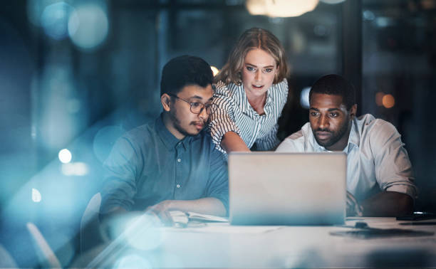 Cropped shot of three young businessmpeople working together on a laptop in their office late at night Showing them the way cooperation stock pictures, royalty-free photos & images