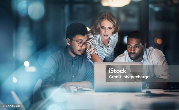 Cropped Shot Of Three Young Businessmpeople Working Together On A Laptop In Their Office Late At Night Stock Photo - Download Image Now