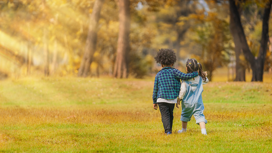 two diverse mixed race children boy and girl have fun playing and running together in park during autumn