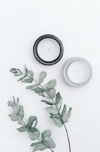 Scented candle in glass jar with natural ingredients on white wooden background with branches of eucalyptus. Wellness and physical, emotional health concept. Flat lay, top view