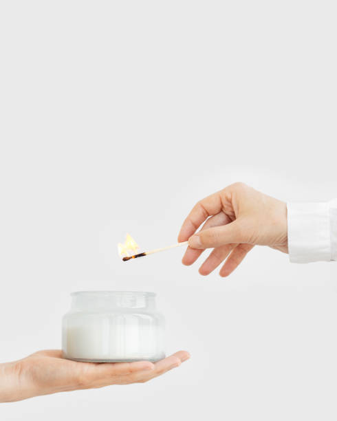 female hand uses matchstick to light fragrant candle in glass jar with natural ingredients - fire match women flame imagens e fotografias de stock