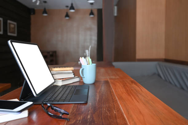 istock Side view mock up computer tablet with empty screen, glasses, books and pencil holder on wooden desk. 1322242935