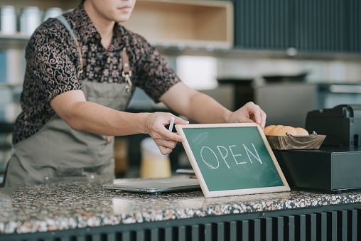 Asian chinese male cafe shop owner using chalk writing on chalkboard blackboard with word open in the morning