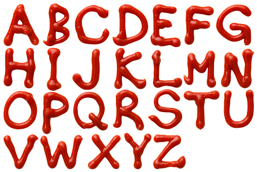 Overhead shot of upper case letters alphabetical order written in ketchup on white background.