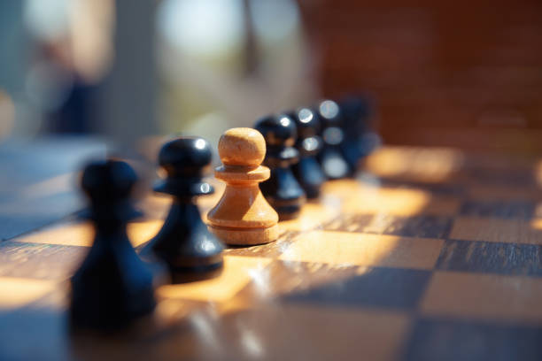 istock A white pawn between black chess pieces on an old chessboard. 1322244883