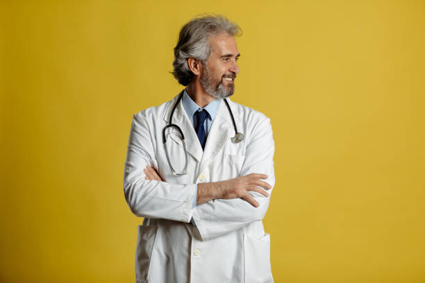 Good health concept. Smiling doctor with crossed arms posing on yellow background and looking a side stock photo