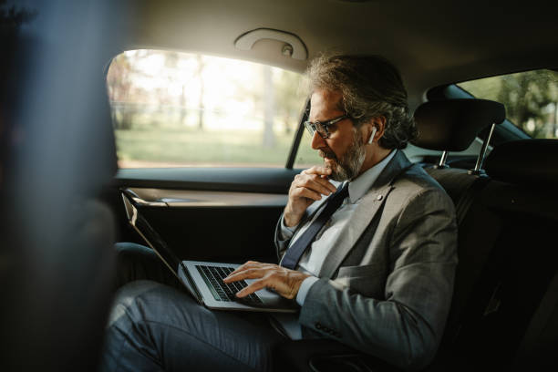istock Handsome businessman working on his laptop while sitting in the car. 1322247803