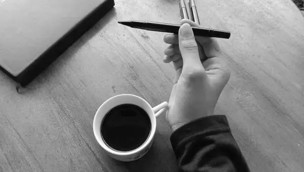 Photo of a person enjoying a cup of black coffee on a wooden table