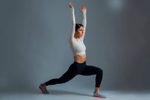 istock Woman in lunging Warrior Pose with arms outstretched up on grey background 1322249051