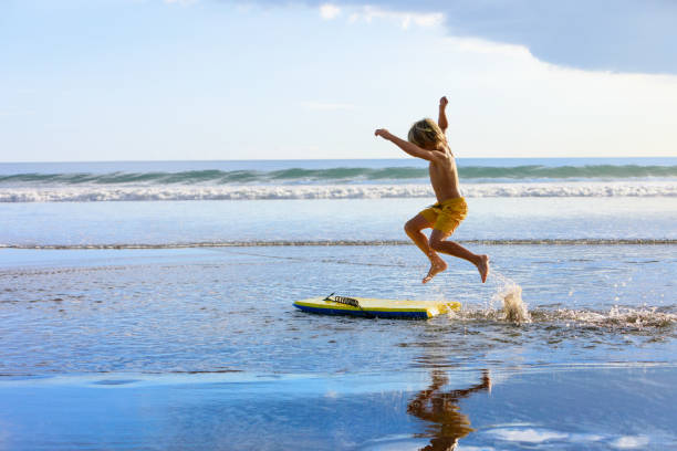 ボディボードを持つ少年は海のビーチで楽しみを持っています - summer swimming beach vacations ストックフォトと画像