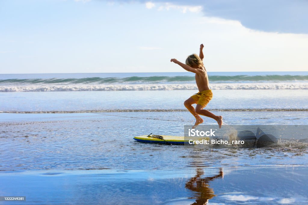 Boy with bodyboard have fun on sea beach Happy boy - young surfer with bodyboard have fun on beach, run by sea water pool. Active family lifestyle, kids outdoor water sports, swimming activity in surf camp. Summer vacation with child. Beach Stock Photo