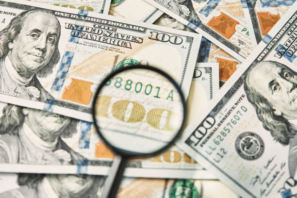 istock Magnifying glass on a pile of 100 dollar banknotes 1322251316