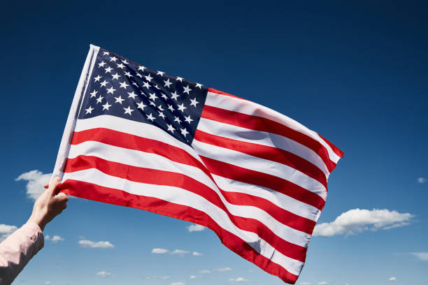 istock Waving usa flag in hand against blue sky 1322251332