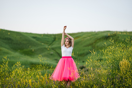 Portrait of a serious girl princess in a country. The girl in a pink dress walks barefoot on the green grass in the field.