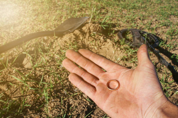 un antico anello d'oro in mano a un cercatore, trovato su un vecchio tratto con l'aiuto di un metal detector, il primo piano e lo sfondo sono sfocati con un effetto bokeh - searcher foto e immagini stock