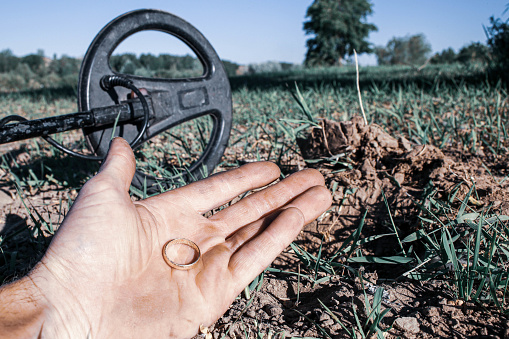 an antique gold ring in the hand of a searcher, found on an old tract with the help of a metal detector, the foreground and background are blurred with a bokeh effect