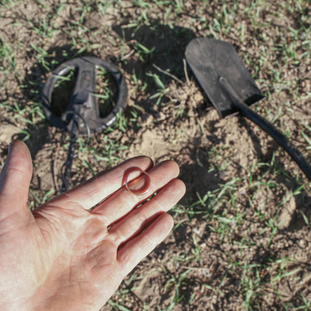 un antico anello d'oro in mano a un cercatore, trovato su un vecchio tratto con l'aiuto di un metal detector, il primo piano e lo sfondo sono sfocati con un effetto bokeh - searcher foto e immagini stock