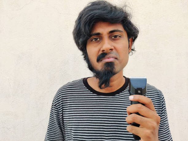 sad face of smart south indian young man with half beard and moustache. holding a trimmer. white background - facial expression child asia asian and indian ethnicities imagens e fotografias de stock