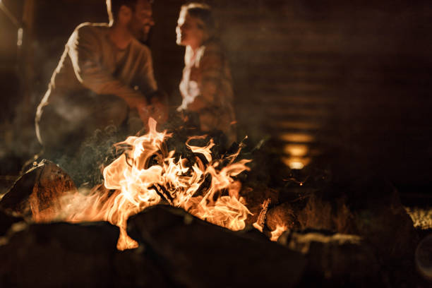 Close up of burning flame of a bonfire by night with couple in the background.