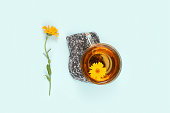Cup of herbal tea on stone and calendula flower on blue background. Calming drink concept