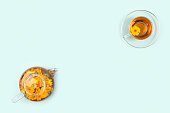 Cups of herbal tea, transparent teapot with calendula flowers on blue background. Calming drink concept. Copy space Flat lay Top view