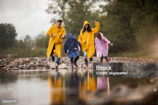 Carefree Family Having Fun While Running Into Water During Rainy Day Stock Photo - Download Image Now