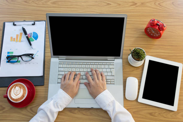 istock Top view female hands working on modern laptop. Office desktop on wooden background 1322262123