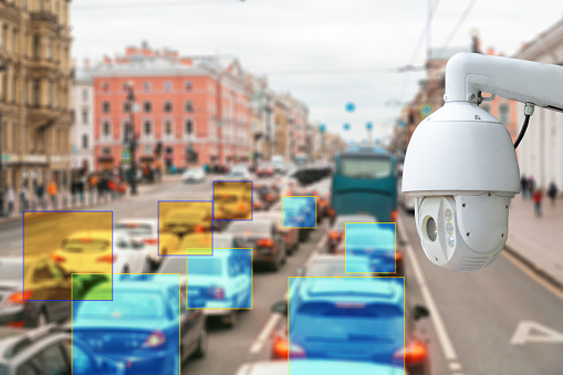 The concept of video surveillance and security technologies. Surveillance camera on the background of the city road with cars.