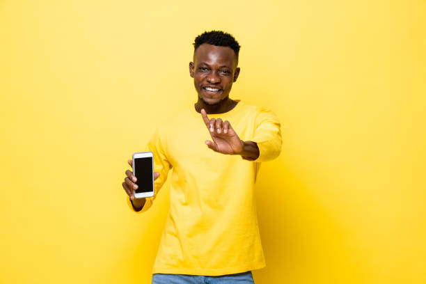 istock Young smiling African man holding mobile phone and doing no gesture in yellow isolated studio background 1322272546