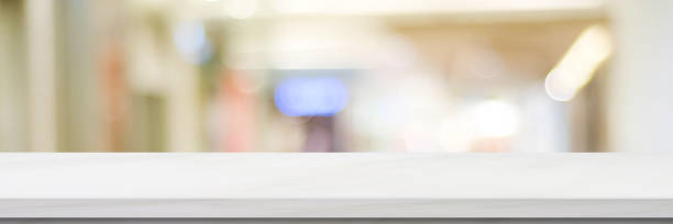 istock Empty white table top, counter, desk over blur perspective store with bokeh light background, White marble stone table, shelf and blurred shop for food, product display mockup, template backdrop, banner, Retail business wallpaper, poster 1322273193
