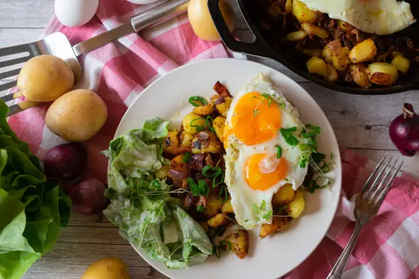 Traditional fried potatoes with fried eggs, sunny side up served with a fresh green salad on a plate. Overhead view with rustic background