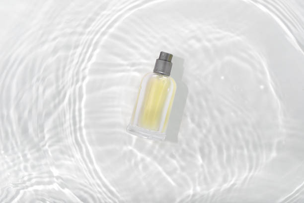 botella de perfume de cosméticos en la superficie de agua salpicada con círculos sobre fondo blanco. diseño de la maqueta de maqueta de paquete de tubo de pulverización de vidrio. - perfume bottle scented cosmetics fotografías e imágenes de stock