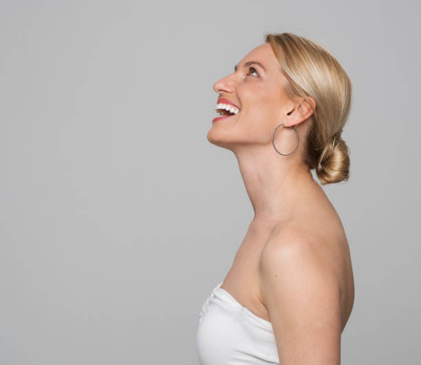 Profile of laughing woman Side view of laughing woman looking up while standing against grey background. hair bun stock pictures, royalty-free photos & images