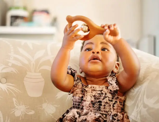 Cute girl sitting on armchair playing with a rattle toy indoors