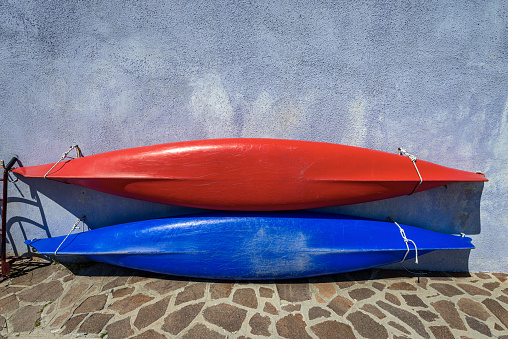 Two canoes or kayaks, one red and the other blue, hanging on the wall hanging of a house in Burano island, Venice lagoon, Veneto, Italy, Europe.