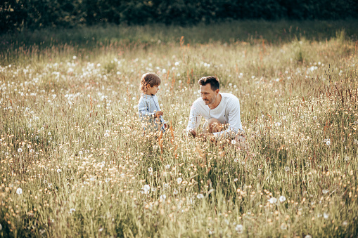 Young dad spending time with his little son in nature, collecting bouquet for mom from wildflowers, fathers day