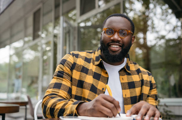 istock Smiling university student studying, exam preparation, taking notes. Education concept. Happy African American business man writing on notebook, working project, planning strategy at workplace 1322285222
