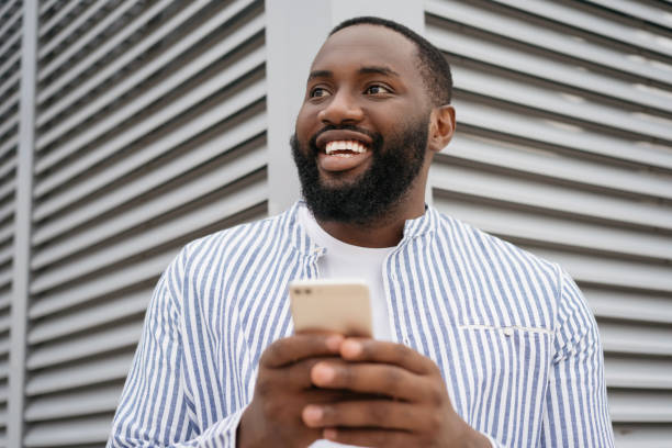 istock Young confident African businessman holding cellphone, communication, working online, standing on the street . Smiling man shopping online 1322285296