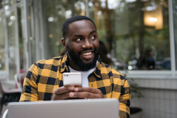 istock Smiling African man holding smartphone, working online. Portrait of young successful developer planning start up, sitting at workplace 1322285928