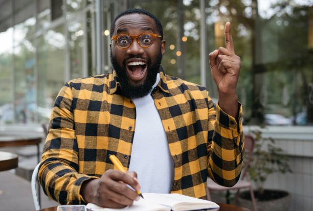 istock Excited African American student studying, learning language, holding finger up, having creative idea. Overjoyed young business man working, taking notes, planning start up 1322285997