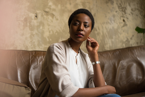 A shot of a young African American woman sitting confidently on the leather sofa.